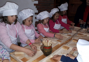 Dzieci w strojach kucharskich rozwałkowują ciasto.